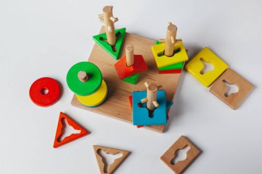Çocuk Montessori oyuncağı oynuyor. Beyaz arka planda çok renkli mantık sıralayıcısı. Bebek Eller yakın çekim. Tahta geometrik şekiller daire, kare, üçgen, dikdörtgen. Yukarıdan görüntüle