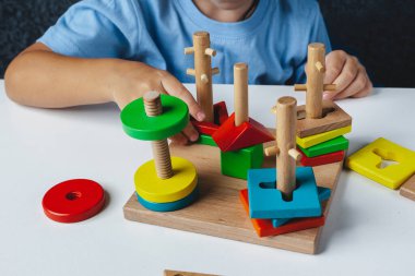 Çocuk Montessori oyuncağı oynuyor. Beyaz arka planda çok renkli mantık sıralayıcısı. Bebek Eller yakın çekim. Tahta geometrik şekiller daire, kare, üçgen, dikdörtgen. Yukarıdan görüntüle