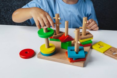 Çocuk Montessori oyuncağı oynuyor. Beyaz arka planda çok renkli mantık sıralayıcısı. Bebek Eller yakın çekim. Tahta geometrik şekiller daire, kare, üçgen, dikdörtgen. Yukarıdan görüntüle