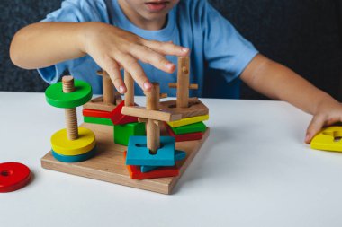Çocuk Montessori oyuncağı oynuyor. Beyaz arka planda çok renkli mantık sıralayıcısı. Bebek Eller yakın çekim. Tahta geometrik şekiller daire, kare, üçgen, dikdörtgen. Yukarıdan görüntüle