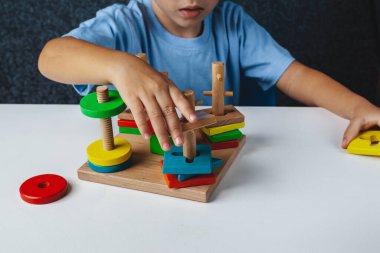 Çocuk Montessori oyuncağı oynuyor. Beyaz arka planda çok renkli mantık sıralayıcısı. Bebek Eller yakın çekim. Tahta geometrik şekiller daire, kare, üçgen, dikdörtgen. Yukarıdan görüntüle