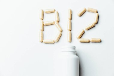  Beyaz arka planda B12 harfi şeklinde haplar, beyaz bir kutudan dökülmüş..