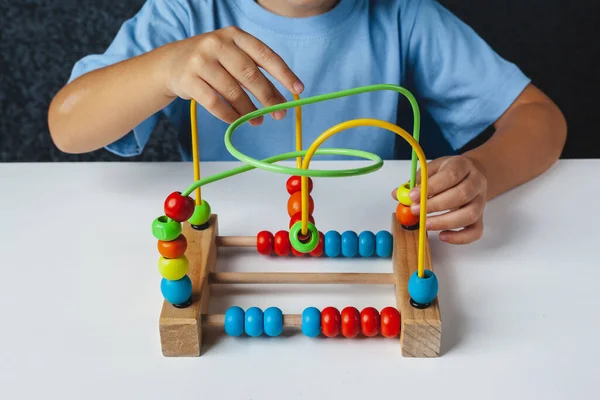 Child plays Montessori game. Kid collects wooden toy sorter. Multicolored geometric  circles and ovals. Early childhood development. Logical maze for the development of fine motor skills.