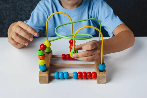 Child plays Montessori game. Kid collects wooden toy sorter. Multicolored geometric  circles and ovals. Early childhood development. Logical maze for the development of fine motor skills.