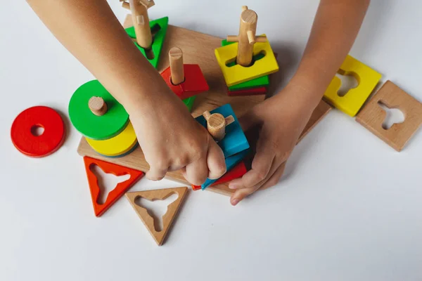 Çocuk Montessori oyuncağı oynuyor. Beyaz arka planda çok renkli mantık sıralayıcısı. Bebek Eller yakın çekim. Tahta geometrik şekiller daire, kare, üçgen, dikdörtgen. Yukarıdan görüntüle