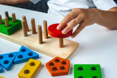 Çocuk Montessori oyunu oynuyor. Çocuk tahta oyuncak ayırıcı topluyor. Çok renkli geometrik şekiller, daire, kare, üçgen, dikdörtgen.