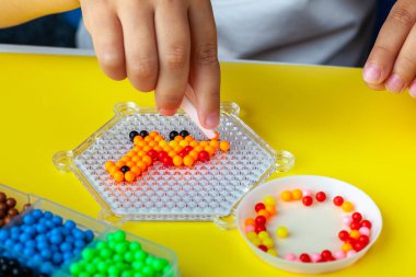 Çocuk eli becerisi, montaj sırasında masada el yapımı su mozaiği, seçici bir odaklanma. Bir çocuk dinozor mozaiği topluyor..