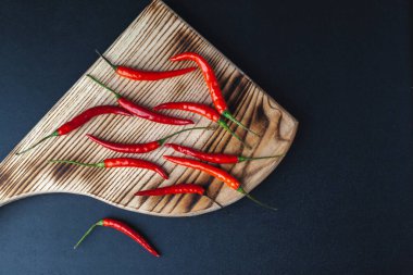 Acı kırmızı biber siyah arka plandaki kesme tahtasının üzerinde yatar. baharatlı kırmızı biber sosu.