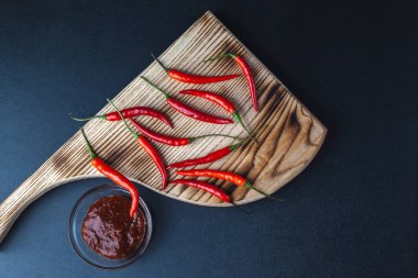 Acı kırmızı biber siyah arka plandaki kesme tahtasının üzerinde yatar. baharatlı kırmızı biber sosu.