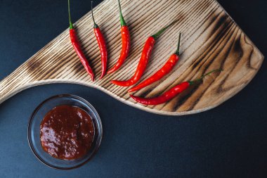 Acı kırmızı biber siyah arka plandaki kesme tahtasının üzerinde yatar. baharatlı kırmızı biber sosu.