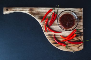 Acı kırmızı biber siyah arka plandaki kesme tahtasının üzerinde yatar. baharatlı kırmızı biber sosu.