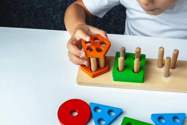 Çocuk Montessori oyunu oynuyor. Çocuk tahta oyuncak ayırıcı topluyor. Çok renkli geometrik şekiller, daire, kare, üçgen, dikdörtgen.