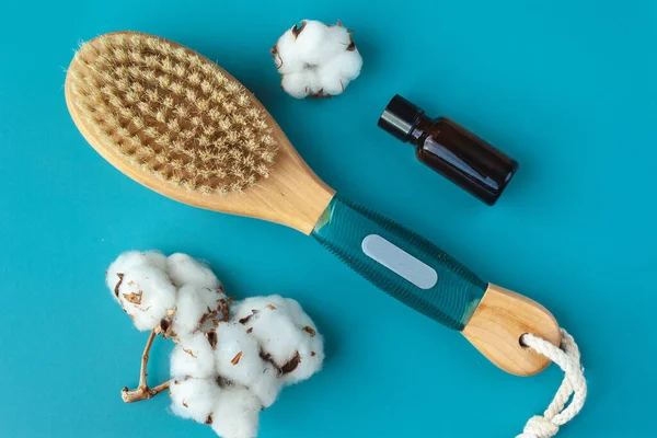Anti-cellulite brush for dry body massage, aromatherapy oil, cotton flowers on a blue background. Lymphatic drainage body massage.