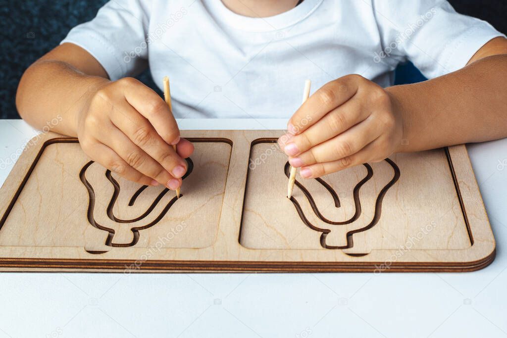 Children's montessori wooden toy. Board for interhemispheric development of the brain. Children's hands close-up. Montessori Games for Child Development. Wooden labyrinth for speech therapist. 