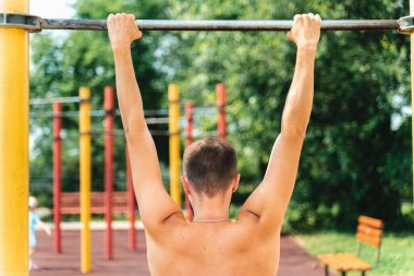 Sporcu kendini yatay çubuğa çekiyor. Parkta spor yapıyor. Sırtında ve boynunda tekila, omurga eğriliği, skolyoz, sırt sorunları.