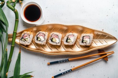 Yaprak şeklinde altın tabakta suşi. Japon yemeği. Yemek çubukları, beyaz tabakta soya sosu. Menü kapağı. Bakış açısı