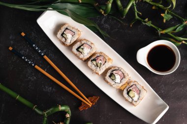Beyaz tabakta taze suşi. Geleneksel Japon yemekleri. Yemek çubukları, soya sosu, siyah arka planda bambu dalları. Asya tarzı