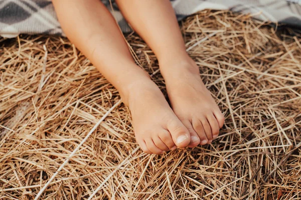 Çocuk samanlıkta oturuyor. Bacaklar yakın. Sonbahar hasadı