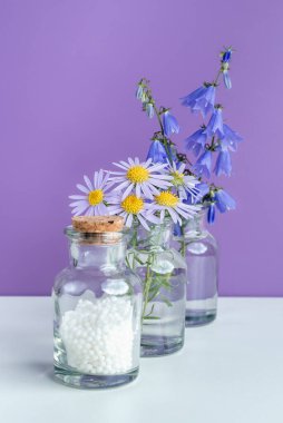 Alternatif şifalı bitkiler ve homeopatik küreseller. Homeopati tıp konsepti. Bir şişe homeopatik boncuk, şifalı bitkiler ve çiçekler. Homeopati ilacı..