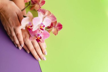 Genç bir kadının elleri yakın plan. Yeşil ve mor arka planda şık moda manikür. Tropik orkide çiçekleri.