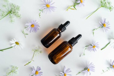 Çiçeklerin arka planında deri sağlığı için bir şişe öz ve surum. Siyah camlı doğal bitkisel cilt bakım ürünleri. Model reklamcılık. Besleyici yüz yağı