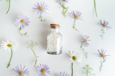 Alternatif şifalı bitkiler ve beyaz arka planda homeopatik küreler. Homeopati tıp konsepti. Bir şişe homeopatik boncuk, şifalı bitkiler ve çiçekler.. 