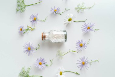 Alternatif şifalı bitkiler ve beyaz arka planda homeopatik küreler. Homeopati tıp konsepti. Bir şişe homeopatik boncuk, şifalı bitkiler ve çiçekler.. 