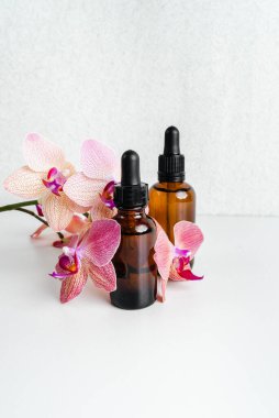 Çiçeklerin arka planında deri sağlığı için bir şişe öz ve surum. Siyah camlı doğal bitkisel cilt bakım ürünleri. Model reklamcılık. Besleyici yüz yağı