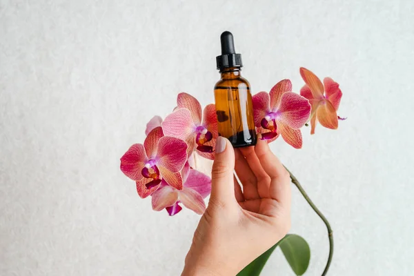 Young woman holds an essence for skin in her hands. Tropical orchid flowers. Unisex cosmetics. Place for  text.  Spa natural organic products.Anti-age cosmetics for men and women.