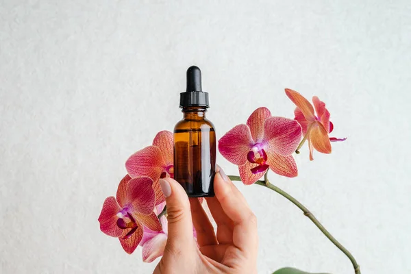 Young woman holds an essence for skin in her hands. Tropical orchid flowers. Unisex cosmetics. Place for  text.  Spa natural organic products.Anti-age cosmetics for men and women.