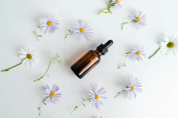 Çiçeklerin arka planında deri sağlığı için bir şişe öz ve surum. Siyah camlı doğal bitkisel cilt bakım ürünleri. Model reklamcılık. Besleyici yüz yağı