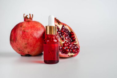 Nar özlü yüz sağlığı için esans. Deri gerdirme için antidepresan kozmetik. Kırmızı cam şişede serum ve nar arkaplanı. Organik Vegan Ürünleri. Metin için yer