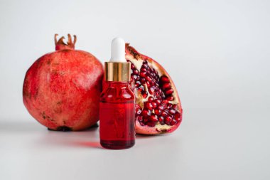 Nar özlü yüz sağlığı için esans. Deri gerdirme için antidepresan kozmetik. Kırmızı cam şişede serum ve nar arkaplanı. Organik Vegan Ürünleri. Metin için yer