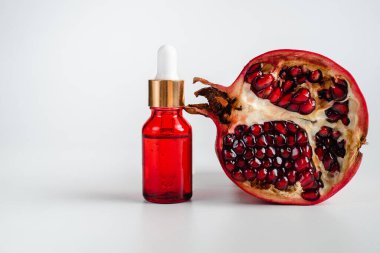 Nar özlü yüz sağlığı için esans. Deri gerdirme için antidepresan kozmetik. Kırmızı cam şişede serum ve nar arkaplanı. Organik Vegan Ürünleri. Metin için yer