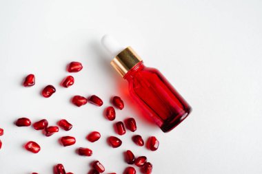 Beyaz arka planda organik nar tohumu özü içeren serum şişesi. Kozmetik doğal serum, cilt bakımı, temel petrol ürünleri. Güzellik ürünleri markası maketi. Düz yatıyordu.