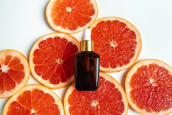 Bottle with essence on background of grapefruit. Organic natural cosmetics product in trendy style.  Anti age cosmetics for skin lifting. Serum in dark glass bottle.  Place for text