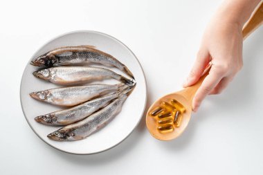 Omega-3 haplı kaşık tutan genç kadın, beyaz arka planda balık yağı ve balık. Sağlık ve bağışıklık için balık yağı kapsülleri. Sağlıklı besinler.