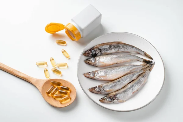 Kaşıkla Omega 3 hapı, balık yağı ve beyaz arka planda balık. Sağlık ve bağışıklık, balık yağı kapsüllerini güçlendiriyor. Sağlıklı yemek.