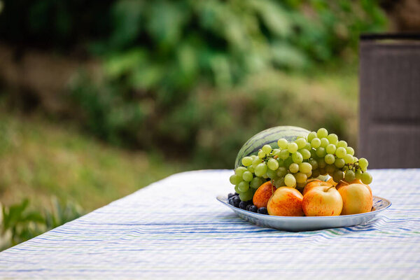 Plate of delicious fresh fruits like watermelon, apples, grapes and blueberries on a table a garden