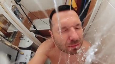 Ağır çekimde, adam banyoda duş alıyor. Duş başlığından görünüm