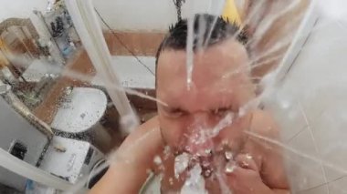 Ağır çekimde, adam banyoda duş alıyor. Duş başlığından görünüm