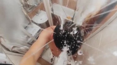 Ağır çekimde, adam banyoda duş alıyor. Duş başlığından görünüm