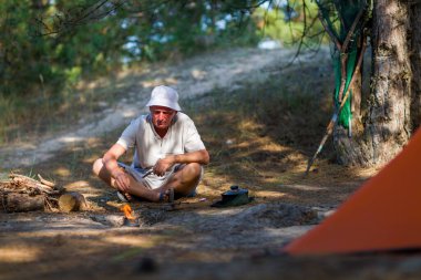Yürüyüşte kamp ateşinde yemek pişiren bir adam..