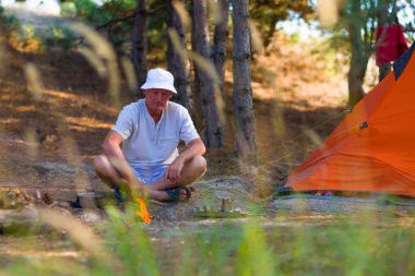 Adam çam ormanındaki çadırın yakınındaki şenlik ateşine bakıyor.