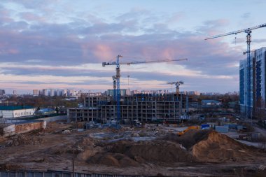 Günbatımında vinçleri ve ağır makineleri olan kentsel inşaat alanı dramatik akşam gökyüzü altında şehir gelişimini, takım çalışmasını ve modern mimari ilerlemesini gösteriyor.