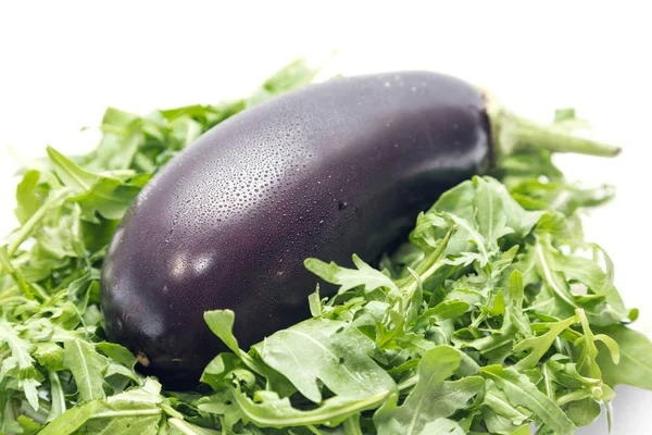 Fresh eggplant with drops of water and rucola on the white background