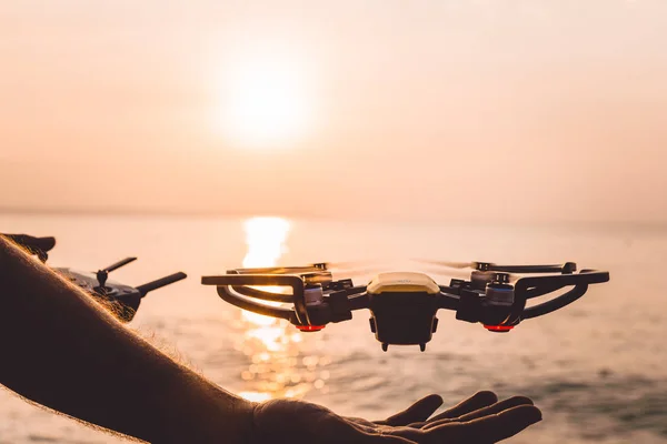 The drone takes off from the pilot\'s hand, at dawn by the sea, the quadrocopter sits on the man\'s hand at sunset by the ocean, piloting a flying drone with a camera, a photographer, a videographer on a journey, a trip to the ocean