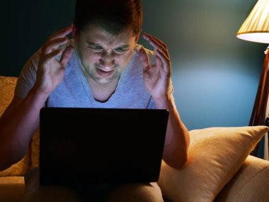 Bir kanepe üstünde laptop korkmuş veya kızgın adam. Akşam saat.