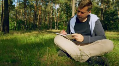 Yong erkek notta yazıyor. Yaz park veya orman.