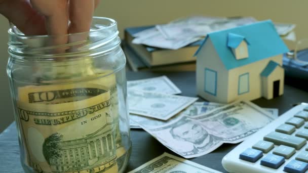 Hände, die Geld in das Gefäß und das Modell des Hauses stecken. Ersparnisse für den Kauf von Immobilien oder Hypotheken.